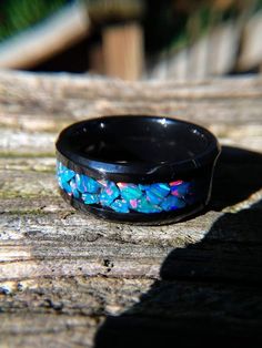 a black ring with blue and pink flowers on it sitting on a piece of wood