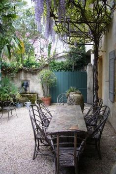 an outdoor dining table and chairs in the middle of a courtyard with wistery trees