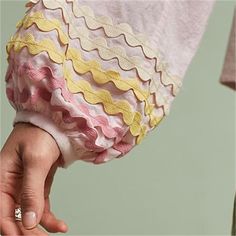 a woman's hand holding onto a pink and yellow dress with ruffles on it