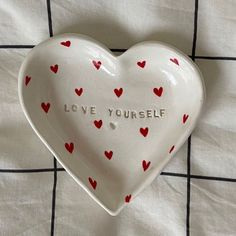 a ceramic heart dish with red hearts on it that says love yourself and is placed on a checkered tablecloth