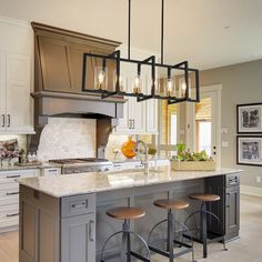 a kitchen island with stools in front of it and lights hanging from the ceiling