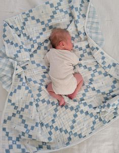 a baby wrapped in a blanket laying on top of a white and blue checkered blanket