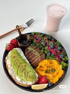 a black plate topped with meat, fruit and veggies next to a drink