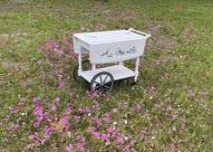 a white cart sitting on top of a lush green field filled with purple wildflowers