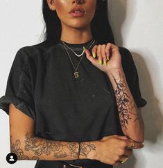 a woman with tattoos standing next to a wall and holding her hand on her hip