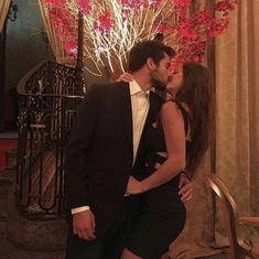 a man and woman are kissing in front of a tree with red flowers on it