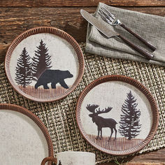 three plates with moose and bear designs on them sitting on a table next to silverware