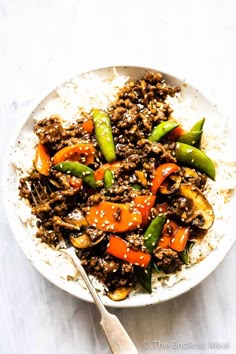 a white bowl filled with rice and vegetables on top of a table next to a fork