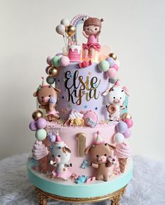 a pink and blue birthday cake with animals on the top is surrounded by other decorations