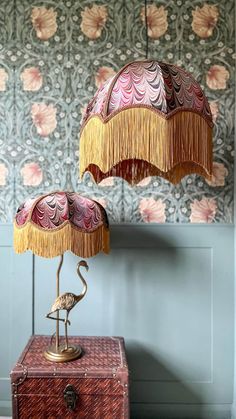 a lamp that is sitting on top of a trunk in front of a wallpapered wall