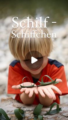 a young boy is playing with scissors on the rocks and leaves in front of him