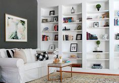 a living room filled with white furniture and lots of bookshelves on the wall