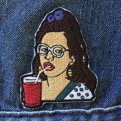 a woman with glasses and a drink in her hand is embroidered onto the back of a jean jacket