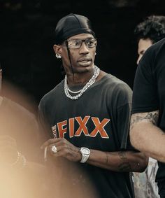 a man wearing a black shirt with the word fix on it, standing next to another man