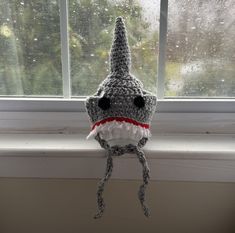 a crocheted stuffed shark hat hanging from a window sill