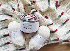 three balls of paintbox yarn sitting on top of a wooden floor next to a white knitted blanket