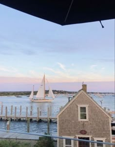 a sailboat is out on the water near a house and dock at sunset or dawn