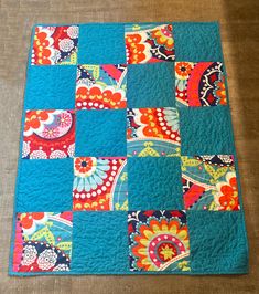 a patchwork quilt on the floor with an orange and blue flowered square pattern