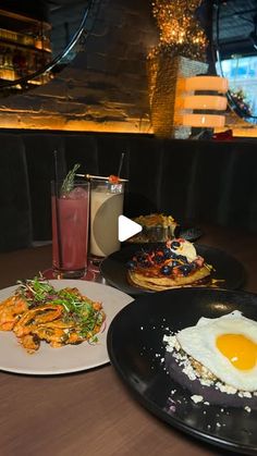 two black plates with food on them sitting on a table next to a glass of drink