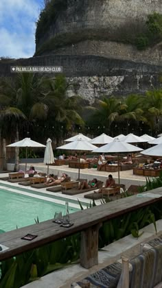 people are lounging at the edge of a swimming pool with umbrellas and lounge chairs