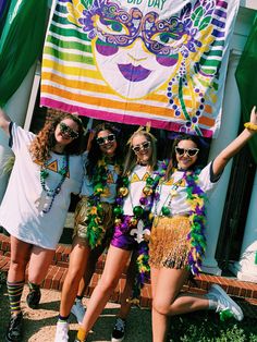 three girls are posing in front of a mardi gras banner