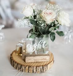 a vase with flowers on top of a wooden table next to a candle and some wine glasses