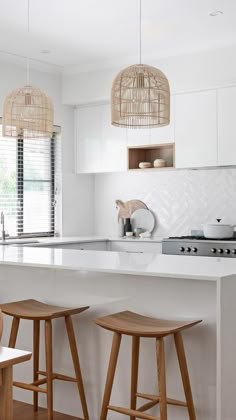 two wooden stools sit in front of an island counter with three pendant lights hanging above it