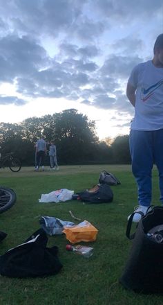 two men standing in the grass with their bikes and bags on the ground next to them