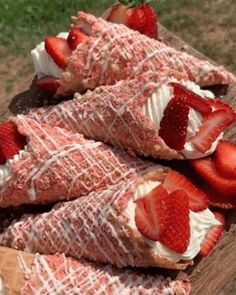 strawberries and whipped cream are arranged on top of a piece of wood that is laying on the ground