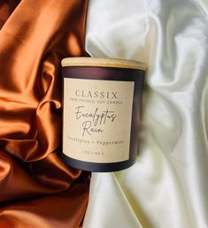 a glass candle sitting on top of a white and orange cloth with the words, classix