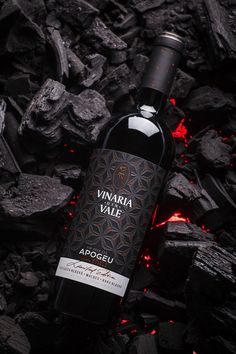 a bottle of wine sitting on top of a pile of rocks next to red lava