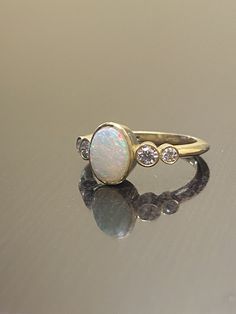 an opal and diamond ring sits on a reflective surface