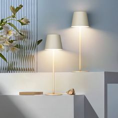 two lamps are next to each other on the wall in front of a vase with flowers