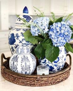 blue and white vases with flowers in them on a tray next to a candle