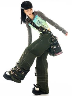 a woman in green pants and black boots posing for the camera with her hand on her hip