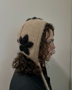 a woman with curly hair wearing a knitted hat and black flower on it's side