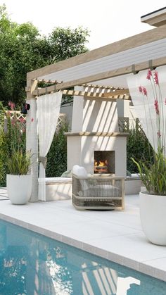 an outdoor fireplace with potted plants next to it and a pool in the background