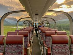 the inside of a train with red seats and mountains in the background at sunset or dawn