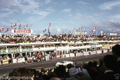 a crowd of people standing around a race track with flags flying in the air and onlookers watching