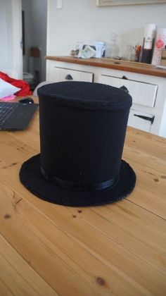 a black top hat sitting on top of a wooden table next to a laptop computer