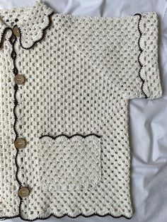 a white knitted sweater with buttons on the front and back, sitting on a bed