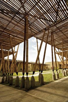 an outdoor covered area with wooden poles and cement vases on the ground in front of it