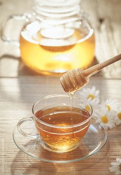 honey being poured into a glass cup on a saucer with daisies in the background