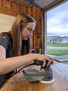 a woman sanding down a wooden table with an electric sander