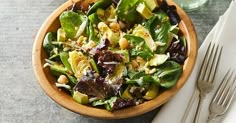 a wooden bowl filled with salad next to silverware