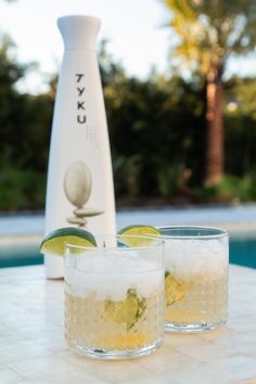 two glasses filled with ice and limes next to a bottle