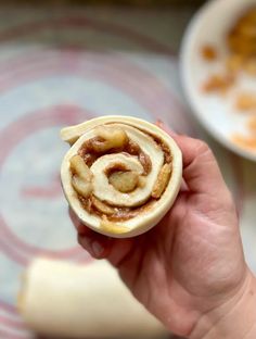 a hand holding a pastry with cinnamon rolls in it's center, on a plate