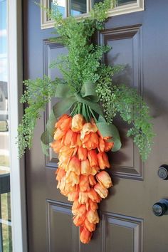 an orange flower hanging on the front door with greenery in it's center