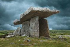 a large rock formation sitting on top of a lush green field under a cloudy sky