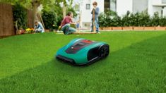 a robotic lawn mower sitting on the grass in front of a house with people standing around